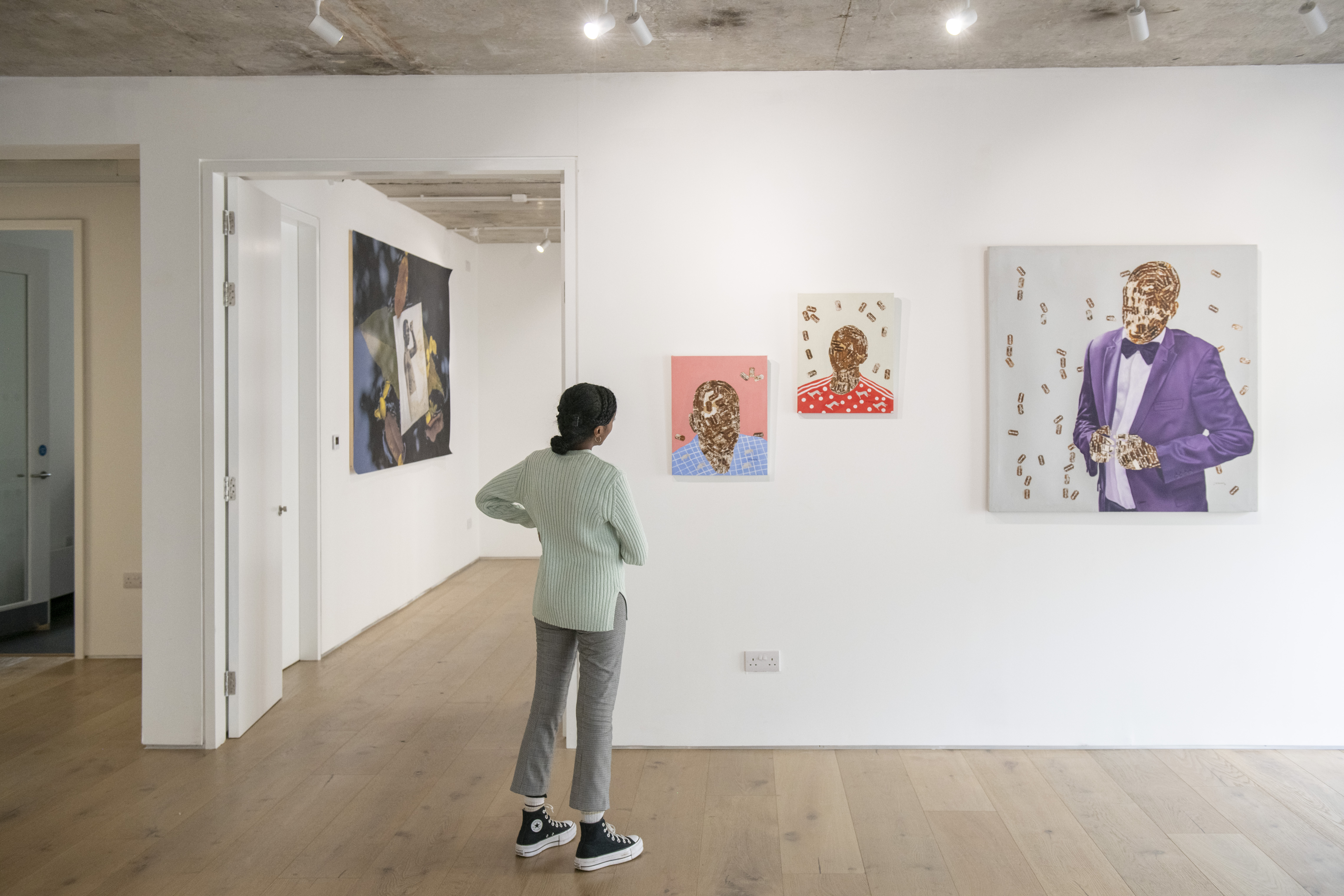 A person gently cocks their head to admire three abstract portrait paintings Black displayed on an art gallery wall.