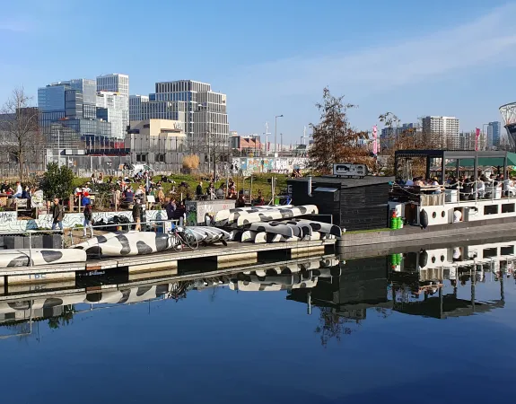 View across the canal at Hackney Wick. People sitting at an outdoor bar area overlooking the Queen Elizabeth Olympic Park and East Bank
