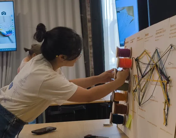Participant at 'There are no "others"' workshop wraps wool around spools stuck to a board