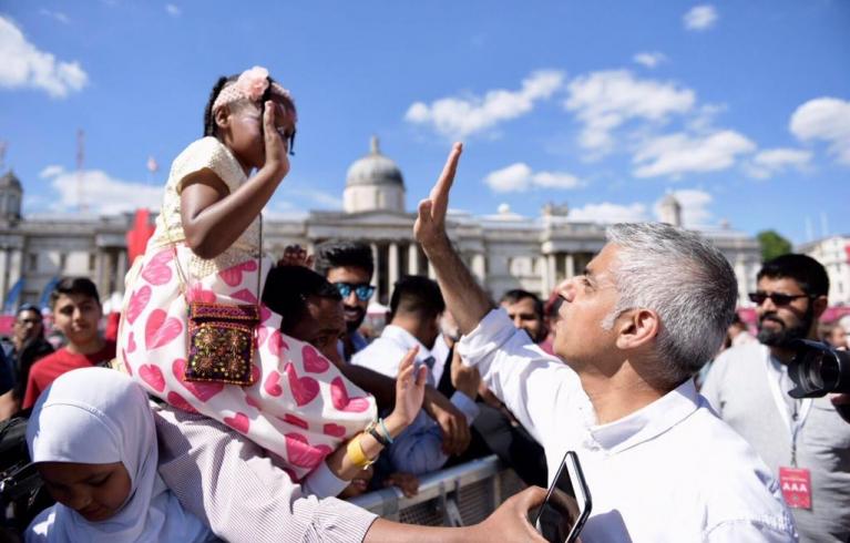Mayor of London, Sadiq Khan, high fiving a child sitting on their parents shoulder at Trafalgar Square during Eid in the Square event