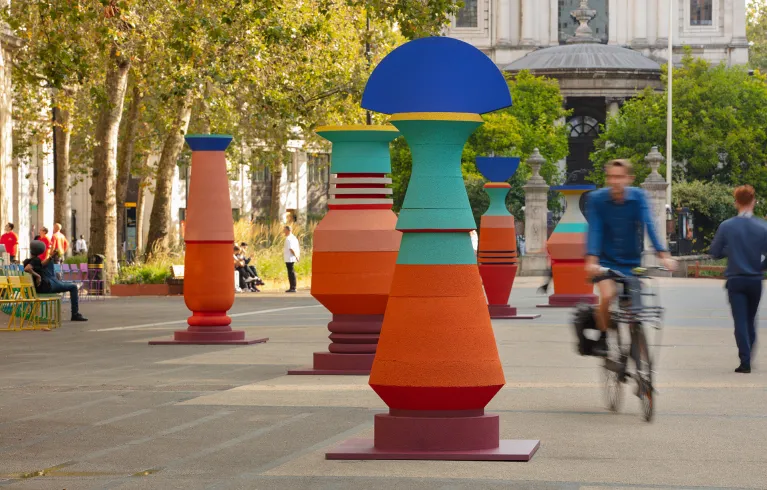 A cyclist rides between brightly coloured vase-like sculptures installed like giant pillars in a public space