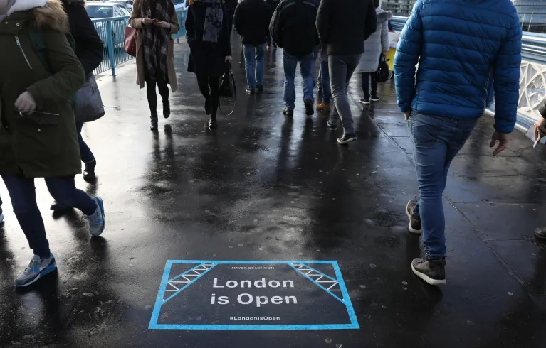A 'London is Open' sticker on the pavement with people walking around it