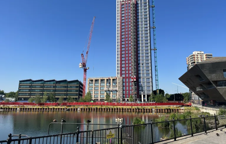 View across water at Canada water towards a construction site of tall buildings and Canada Dock Boardwalk