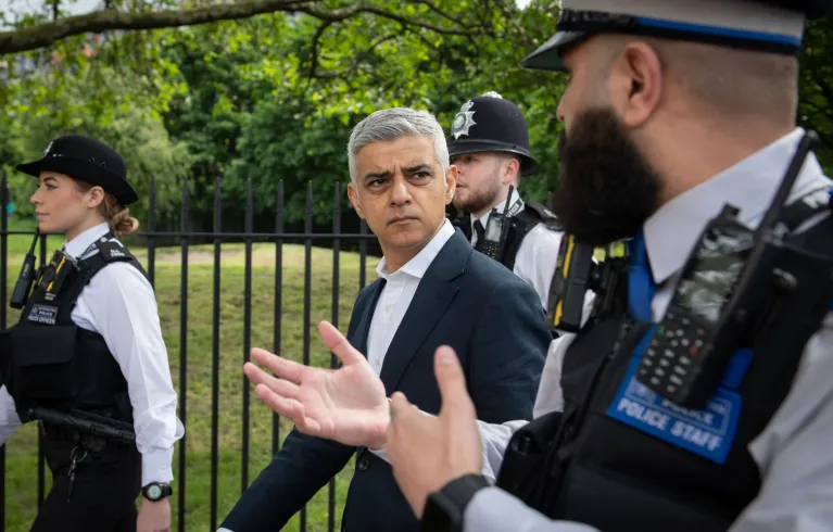 Mayor of London, Sadiq Khan, talking to a police officer as they walk past a park