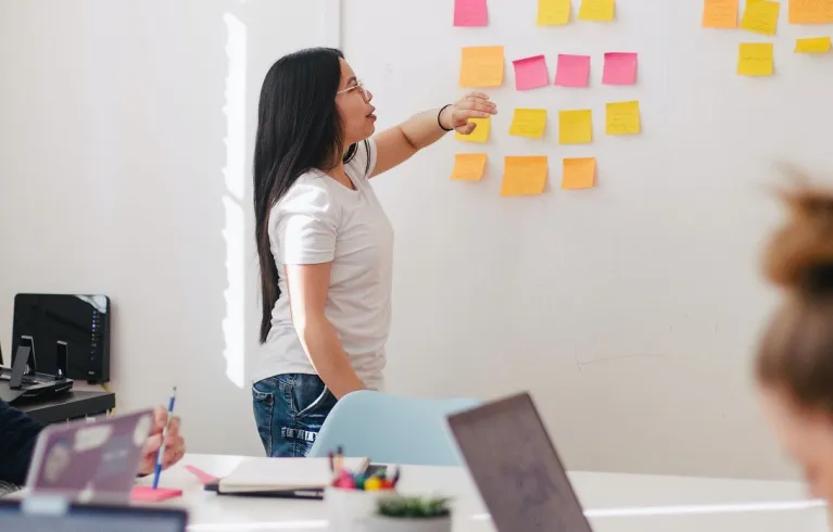 Team discussing comments on post it notes on a whiteboard