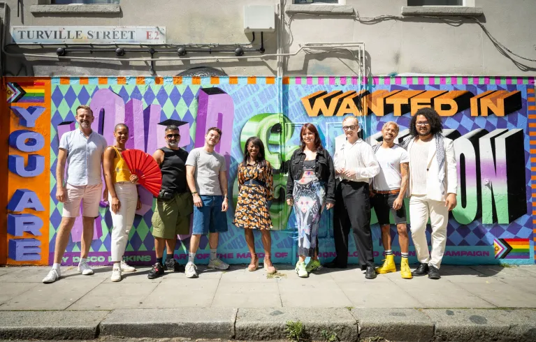 People standing in front of Loved and Wanted pride mural