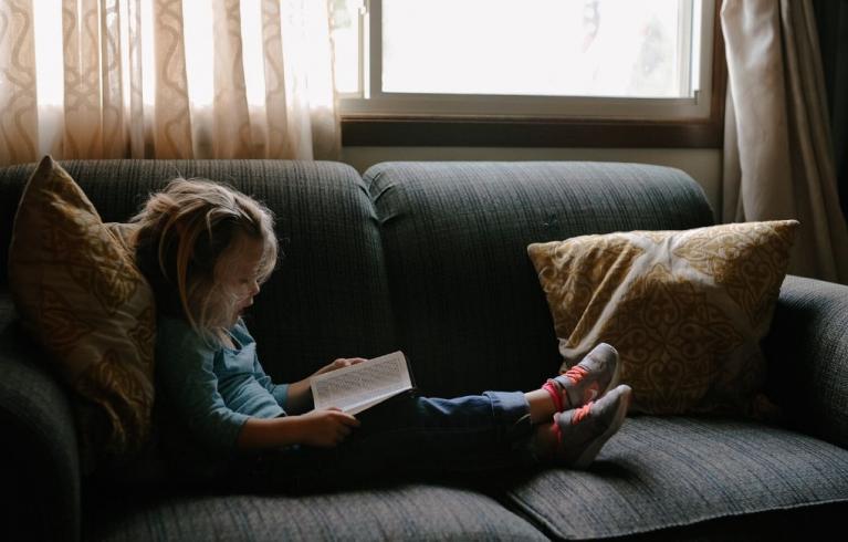 Child reading book on sofa. Photo by Josh Applegate on Unsplash. 