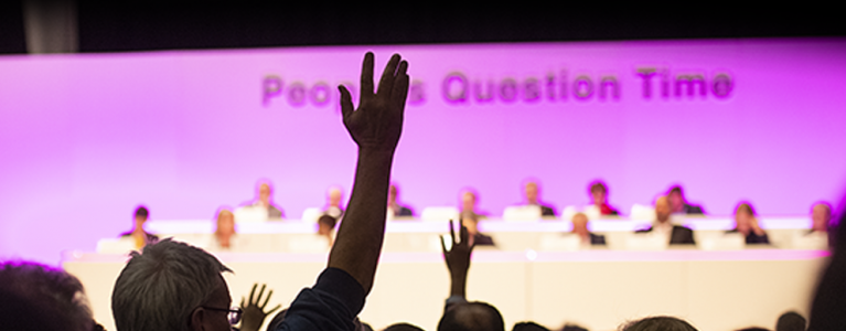 One person is raising his hands from the audience at people's question time event  