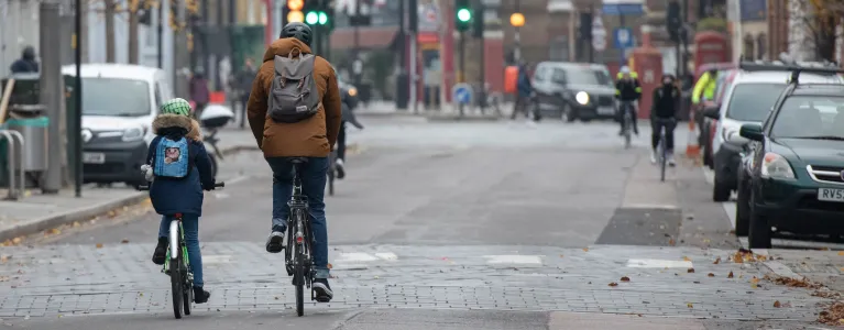 An adult cycling with their child on a London road