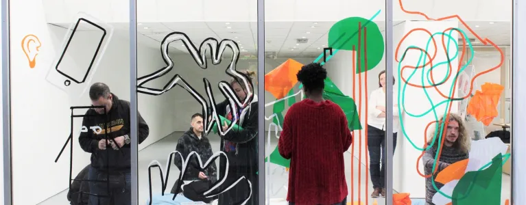 an empty shop front, with people standing on either side drawing and adding designs to the glass panes