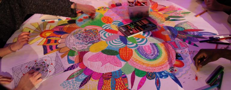 A group of participants colouring in a large illustration on a table during the Rewire summit.