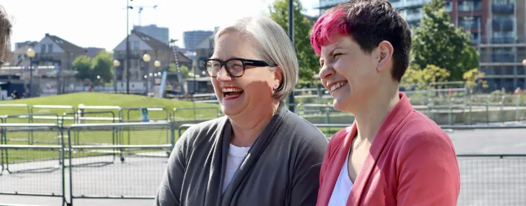 Zoe Garbett and Caroline Russell standing outside of City Hall smiling at a Londoner. 