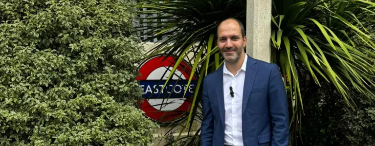 Assembly Member Bassam Mahfouz standing in front of the Eastcote TfL roundel sign, with plants and greenery surrounding him