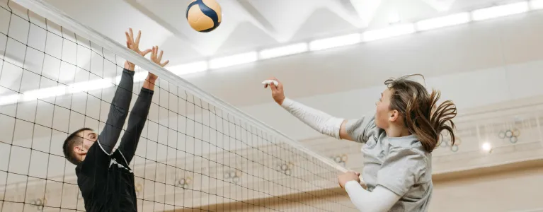 Two people playing volleyball at an indoor location.