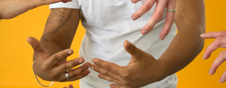 close up of a chest wearing a white tshirt, arms making an open hugging gesture in the air, other hands reach in and around it is a soft and caring way