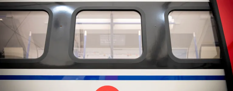 An image of a London tube railcar taken from the outside of the carriage. There are three windows visible, as well as the iconic TfL logo. 