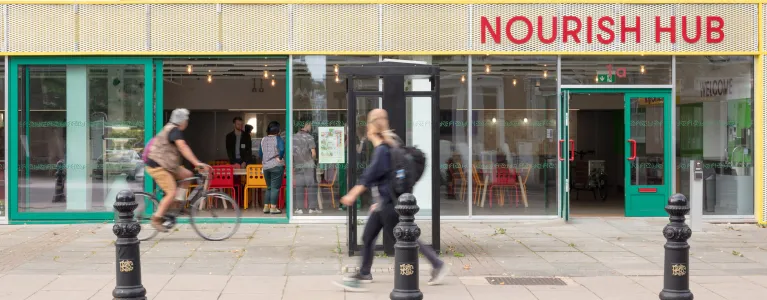 Exterior photo of the front of Nourish Hub, a community food hub kitchen, on the high street, with people walking by