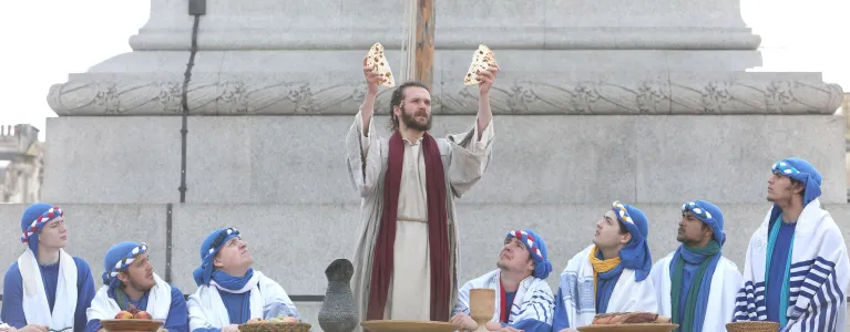 Actor portraying Jesus raises bread at supper with disciples