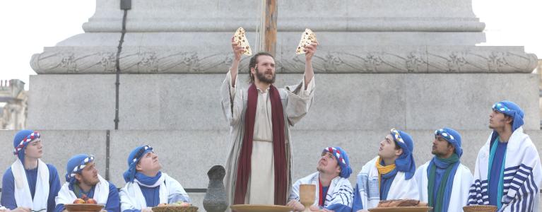 Actor portraying Jesus raises bread at supper with disciples