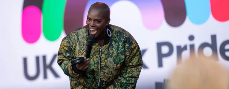Host on stage with microphone, smiling against UK Black pride rainbow backdrop