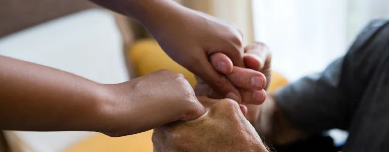 A carer supports an older person, holding their hands.
