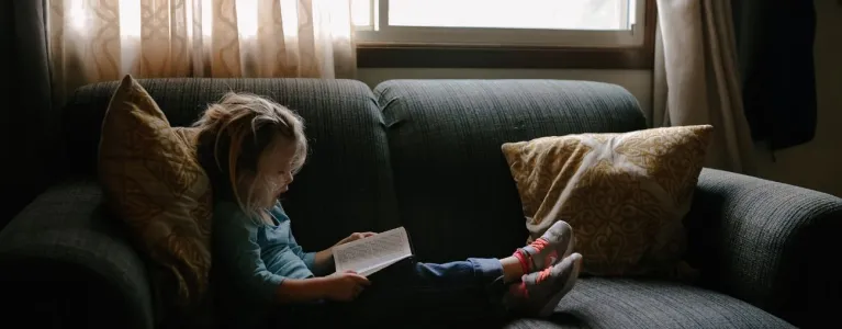 Child reading book on sofa. Photo by Josh Applegate on Unsplash. 