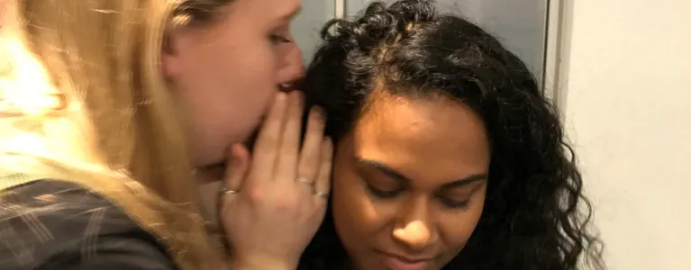 A young woman whispers in anothers ear
