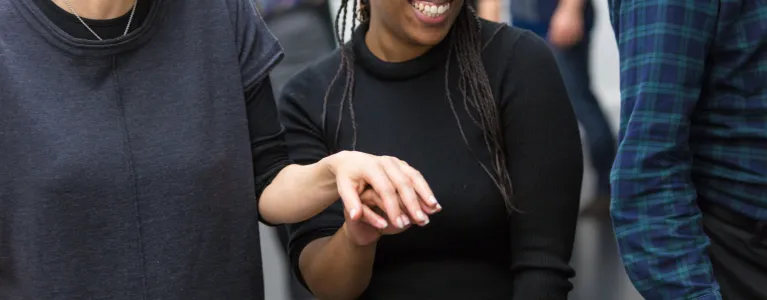 a pair of women are lightly holding hands, smiling and looking ahead of them with anticipation