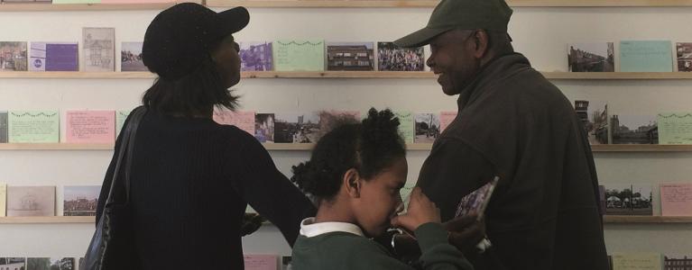 Three people looking at postcards at a community event