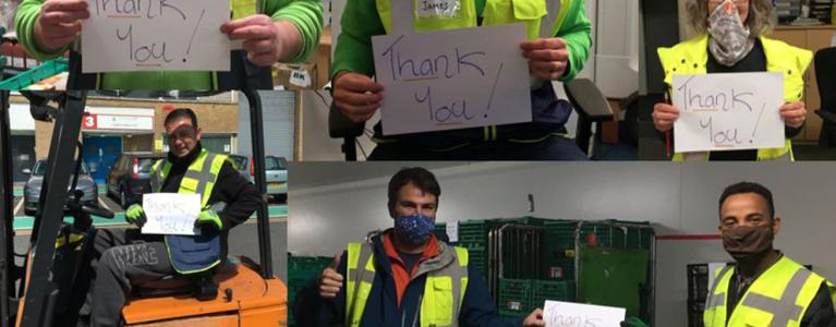 Volunteers wearing high-visibility vests hold up a piece of paper that reads ‘Thank you’