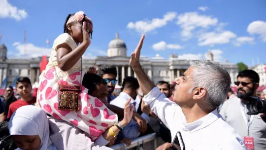 Mayor of London, Sadiq Khan, high fiving a child sitting on their parents shoulder at Trafalgar Square during Eid in the Square event