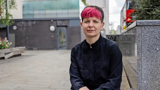 Zoë Garbett AM seated outside in London, staring stern faced at the camera