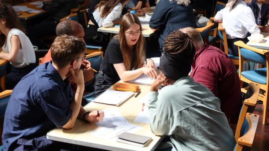Small groups of people sat at tables with notebooks and pens discussing the High Street Network at a study visit.