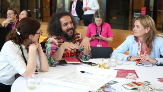 Three people in conversation at a table with printed materials on the table