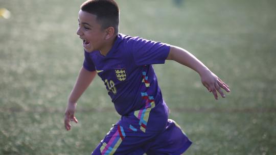 A boy in purple football gear running on a football pitch.