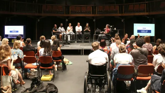 The five case study speakers sit on stalls on stage, while Jame Lee is to their right chairing. The audience clap and sign silent applause as the quickfire case study session comes to a close.