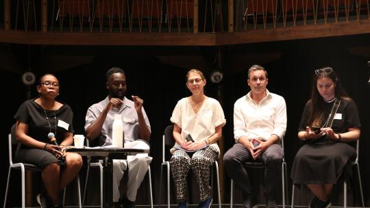 Five case study speakers sit on stalls on stage. The second person along signs to the audience while the others listen to the BSL interpreter.