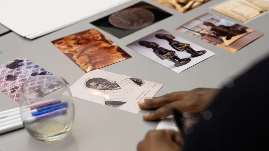 Printed photographs laid on a table. The images show people, art and items related to transatlantic slavery.