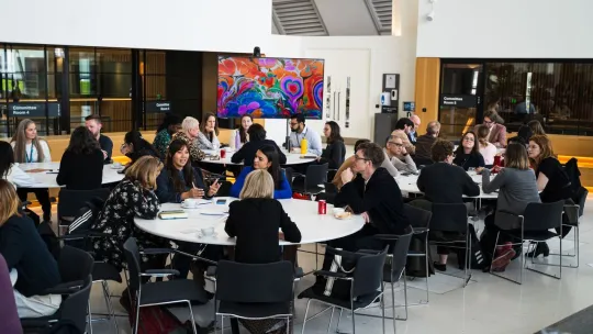 Small groups of people talking while sitting at round tables in a conference room
