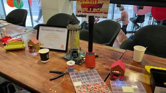 Oasis Waterloo Summer Wrap-Up Party. A desk displaying a sign which reads Creative Wellbeing with boxes of beads on the table