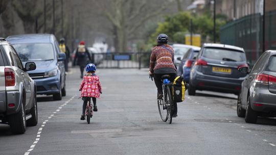 A parent and their child, cycling on a road.