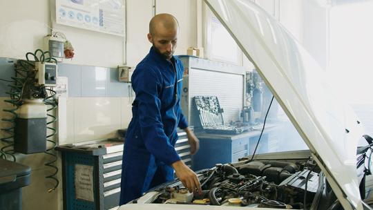 A mechanic working on a car with its bonnet open.