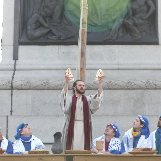 Actor portraying Jesus raises bread at supper with disciples