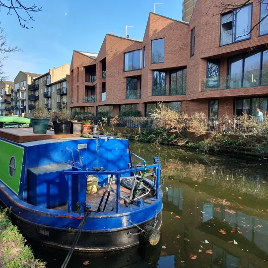 Moored blue and green canal boat with mixed architecture to the opposite side of the canal.
