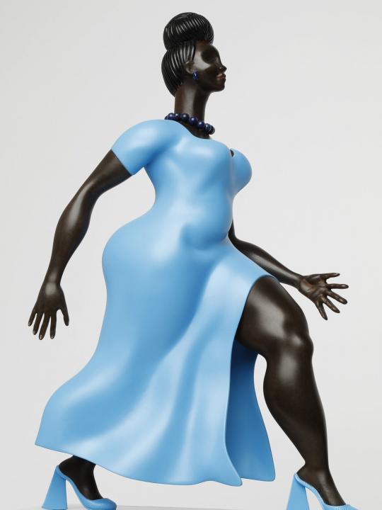 Figure or a black woman, in a blue dress and blue shoes, walking forward, on a light grey plinth, side, close up view