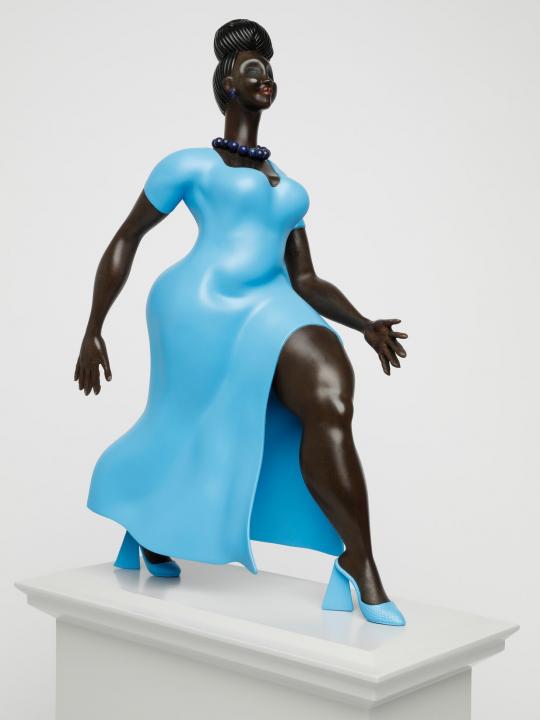 Figure or a black woman, in a blue dress and blue shoes, walking forward, on a light grey plinth, side angled, close up view