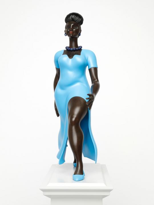Figure or a black woman, in a blue dress and blue shoes, walking forward, on a light grey plinth, front on view