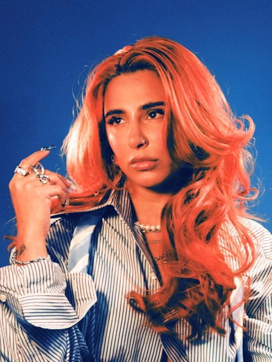 Person with long hair posing for the camera with a blue background.