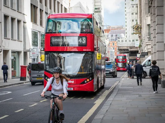 A red London bus and a cyclist on a London street