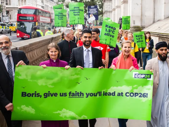 An image showing faith leaders and representatives holding a COP26 banner march towards Downing Street